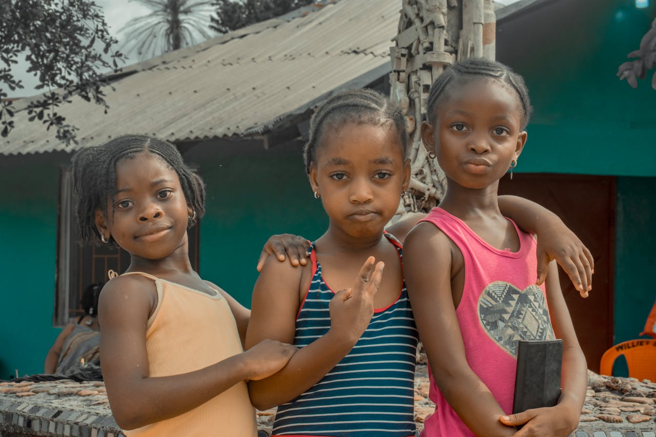 A group of three smiling African children posing together outdoors in Liberia.